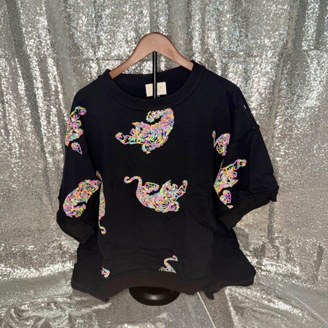 Black top with colorful tiger designs on a hanger against a silver sequin background