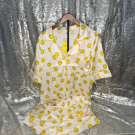 White satin short pajamas with yellow smiley face patterns on a hanger against a silver curtain background